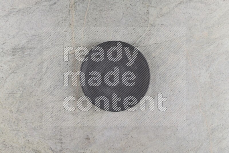 A circular black pottery plate on grey marble background