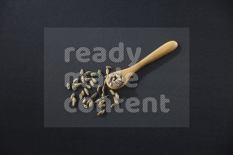 A wooden spoon full of cardamom on black flooring