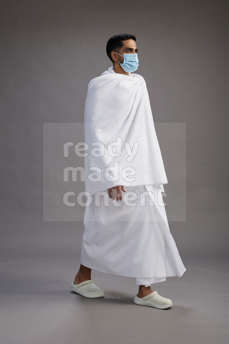 A man wearing Ehram with face mask Standing Interacting with the camera on gray background