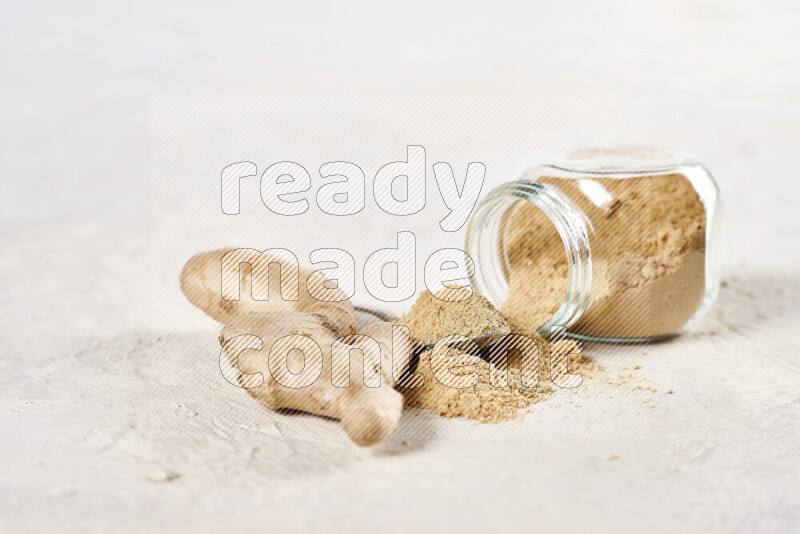 A glass jar full of ground ginger powder flipped with some spilling powder on white background