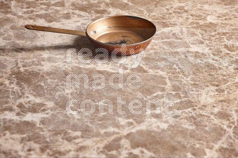 A small copper pan on beige marble background