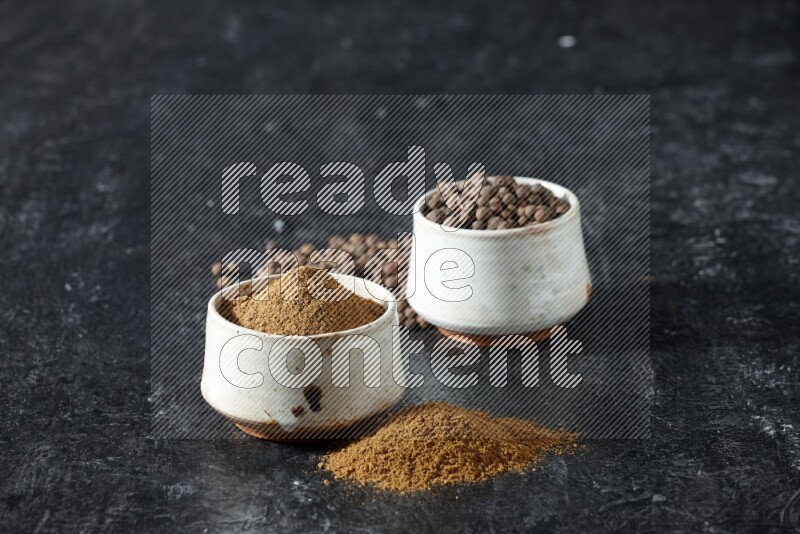 وعاءان بيج، أحدهما ممتلئ ببودرة بهار الفلفل الحلو والآخر بالحبوب وكلاهما متناثران على خلفية سوداء