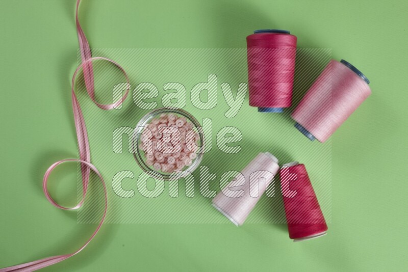 A pink collection of sewing and tailoring tools arranged on a green background