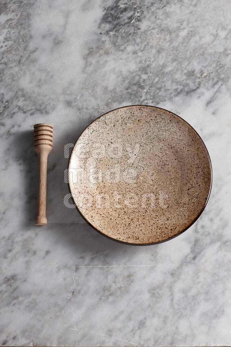 Multicolored pottery plate with wooden honey dipper on the side on grey marble background