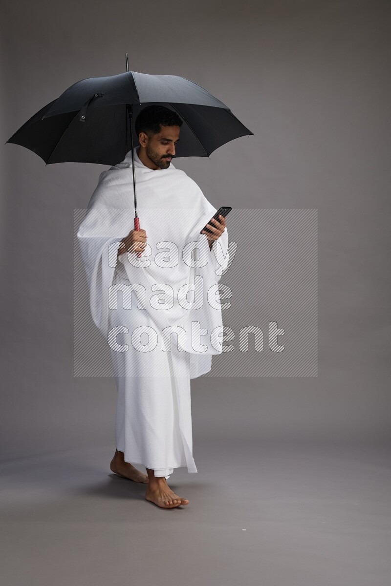 A man wearing Ehram Standing holding umbrella on gray background