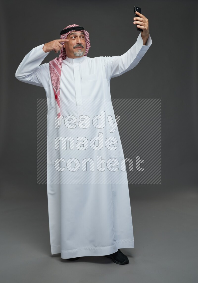Saudi man with shomag Standing taking selfie on gray background