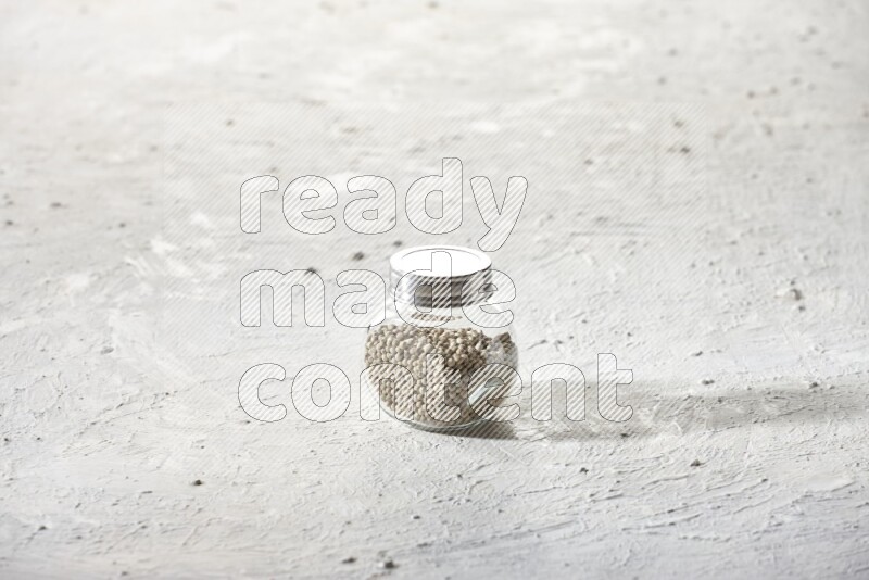 Herbal Glass jar full of white pepper beads on textured white flooring