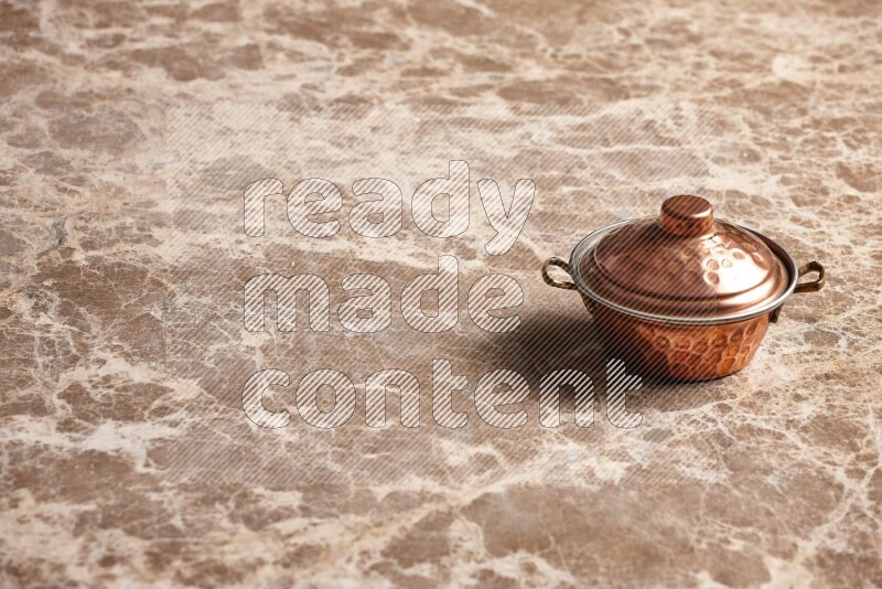 A small copper pot on beige marble background