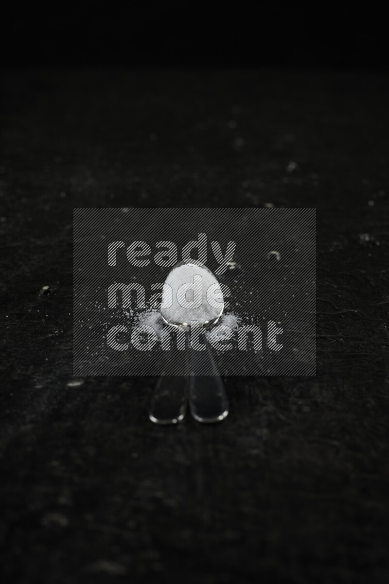 2 metal spoons filled with white salt on black background