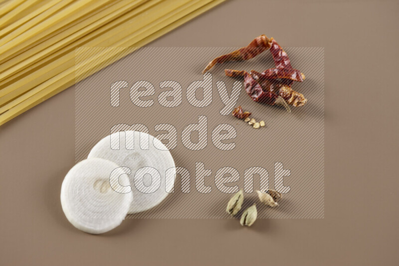 Raw pasta with different ingredients such as cherry tomatoes, garlic, onions, red chilis, black pepper, white pepper, bay laurel leaves, rosemary and cardamom on beige background