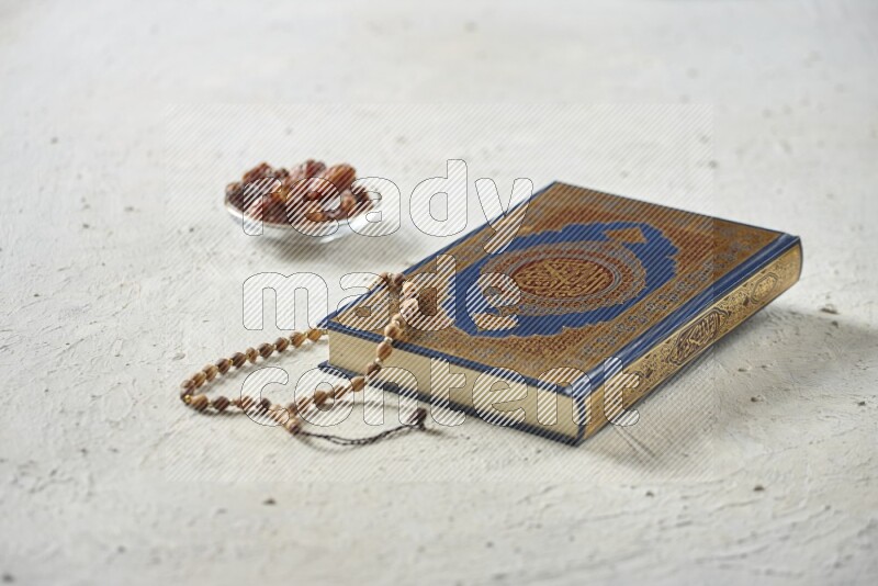 Quran with dates, prayer beads and different drinks all placed on textured white background