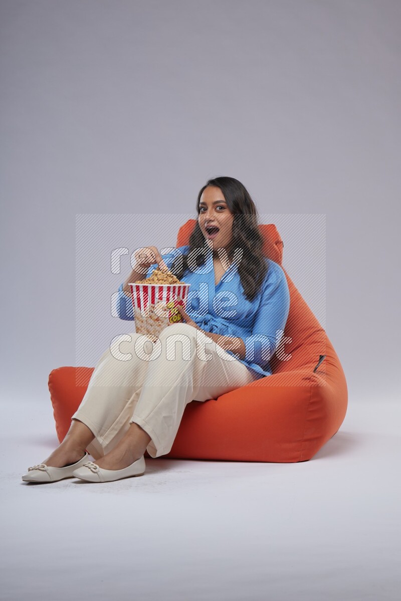 A woman sitting on an orange beanbag and eating popcorn