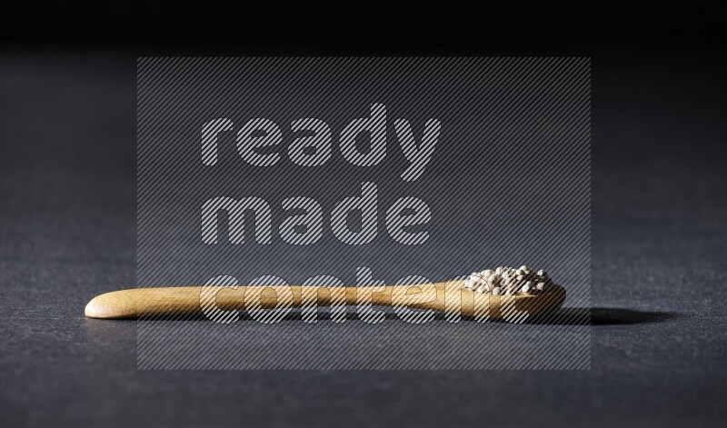 ملعقة خشبية مملوءة بحبات الفلفل الأبيض على أرضية سوداء