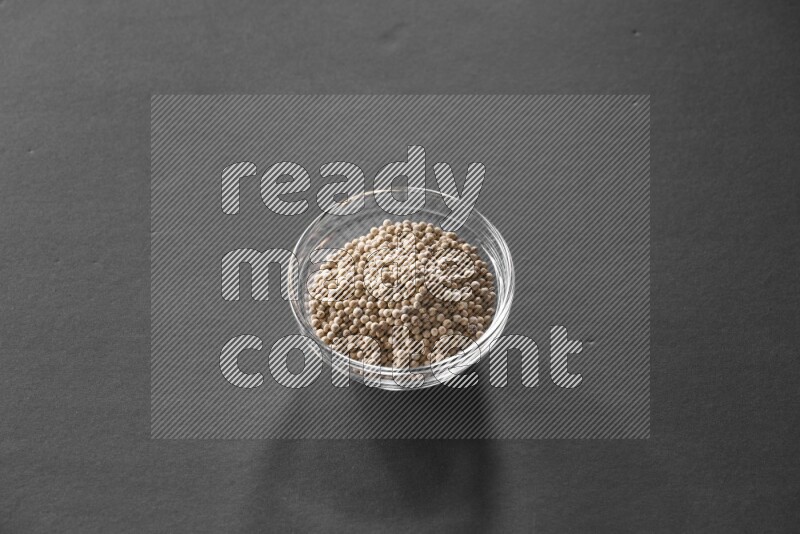 A glass bowl full of white peppers on black flooring