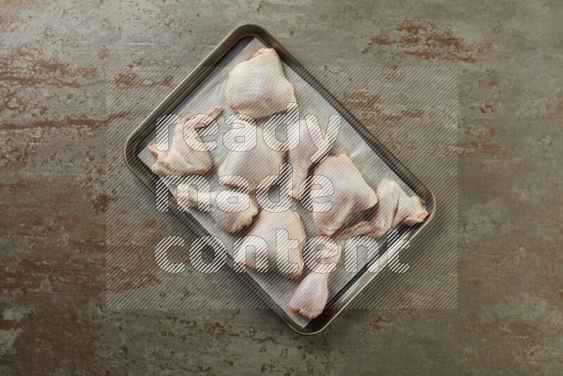 Mixed fresh chicken pieces in an oven tray on a textured rustic background