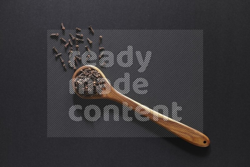 A wooden ladle full of whole cloves on a black flooring