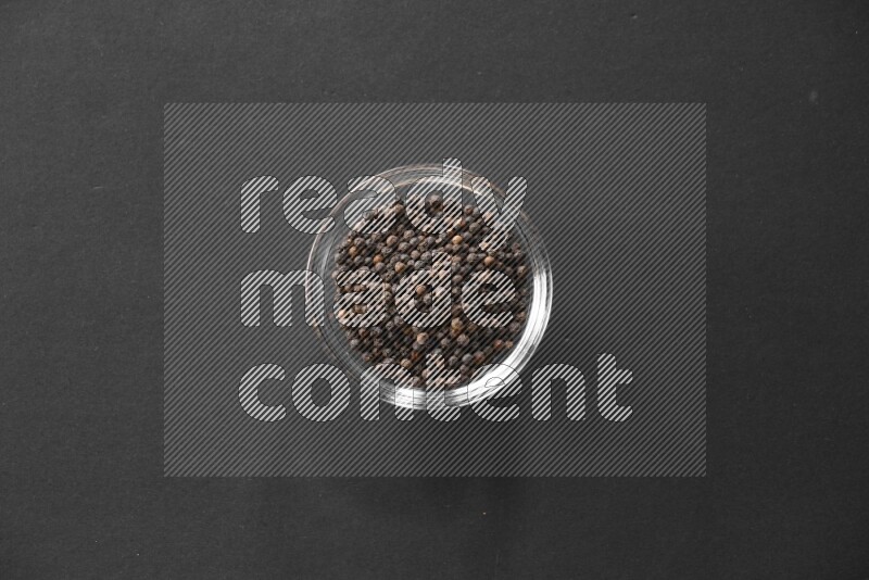 A glass bowl full of black peppers on black flooring