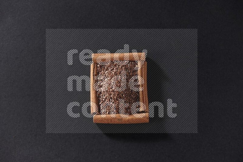 A single square of cinnamon sticks full of flaxseeds on black flooring