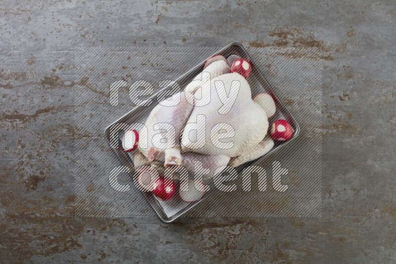 whole Raw chicken on a small oven trey direct on a rustic grey background