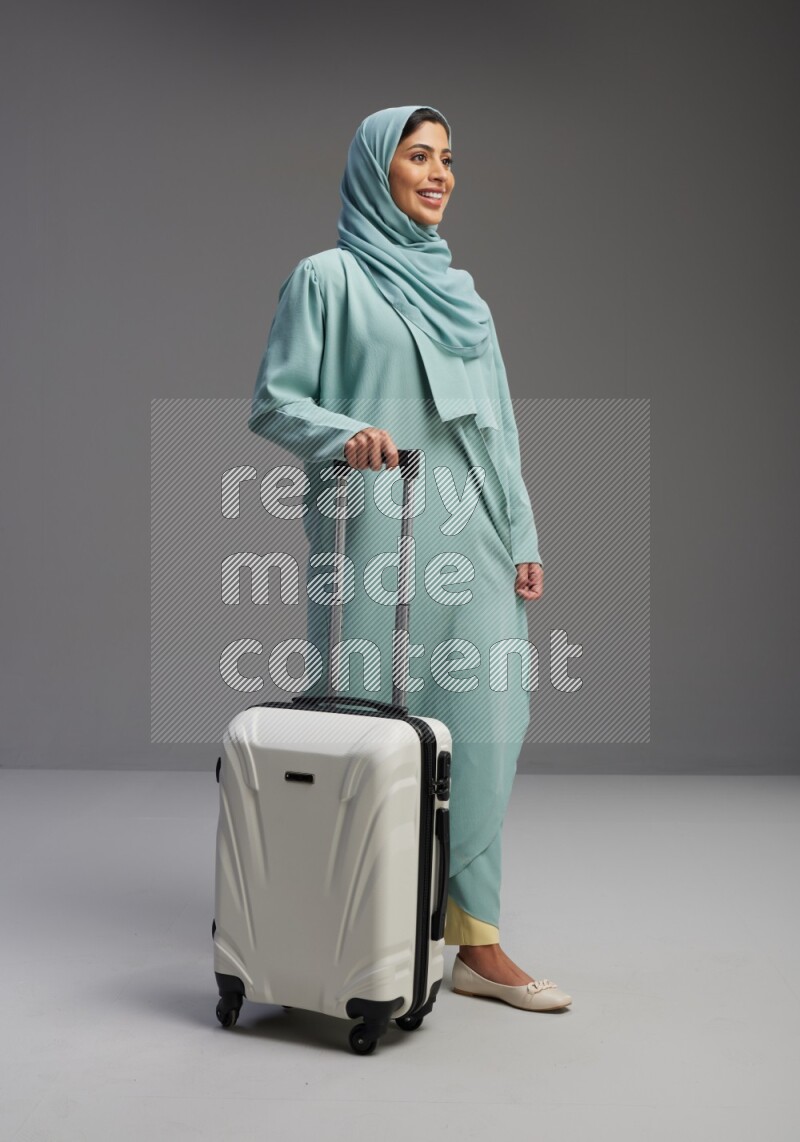 Saudi Woman wearing Abaya standing holding Travel bag on Gray background