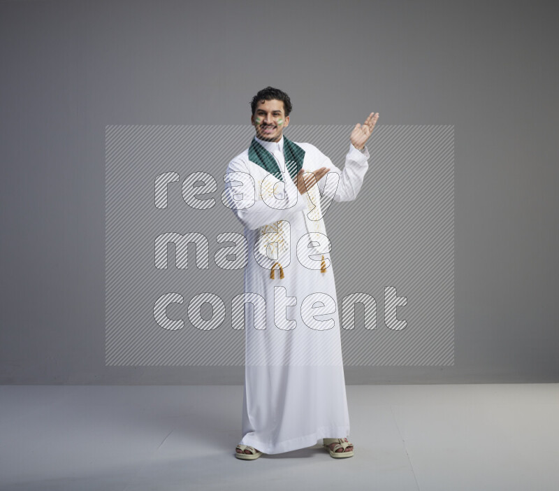 رجل سعودي يرتدي ثوب ابيض يضع شال مكتوب عليه المملكة العربية السعودية حول رقبته