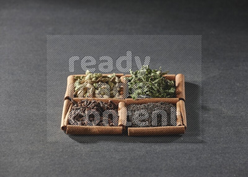 4 squares of cinnamon sticks full of black tea, cloves, dried mint leaves and cardamom on black flooring
