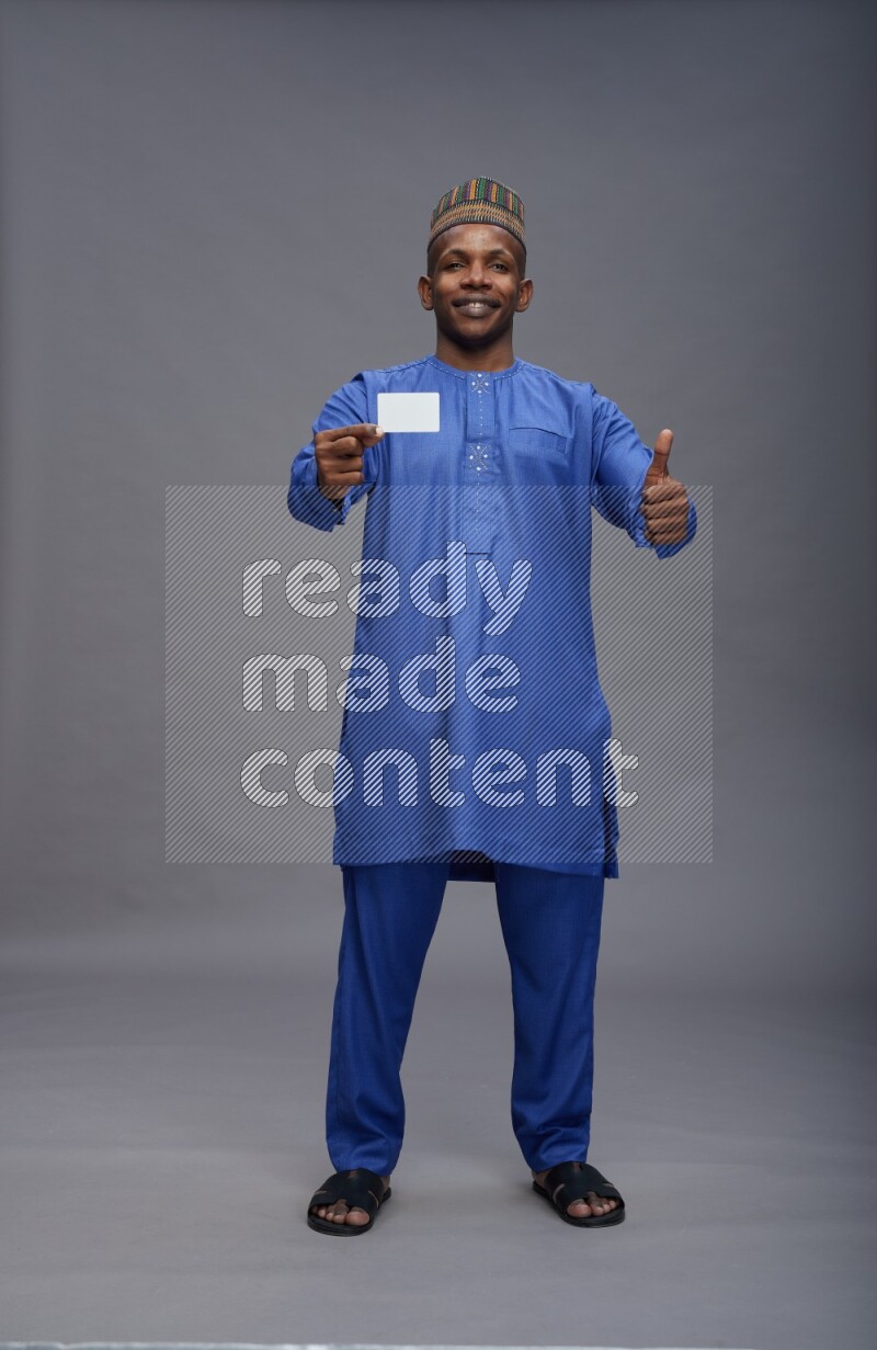 Man wearing Nigerian outfit standing holding ATM card on gray background