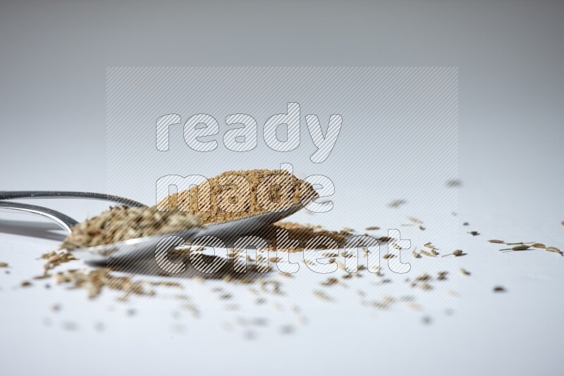 2 metal spoons full of cumin seeds and powder on white flooring