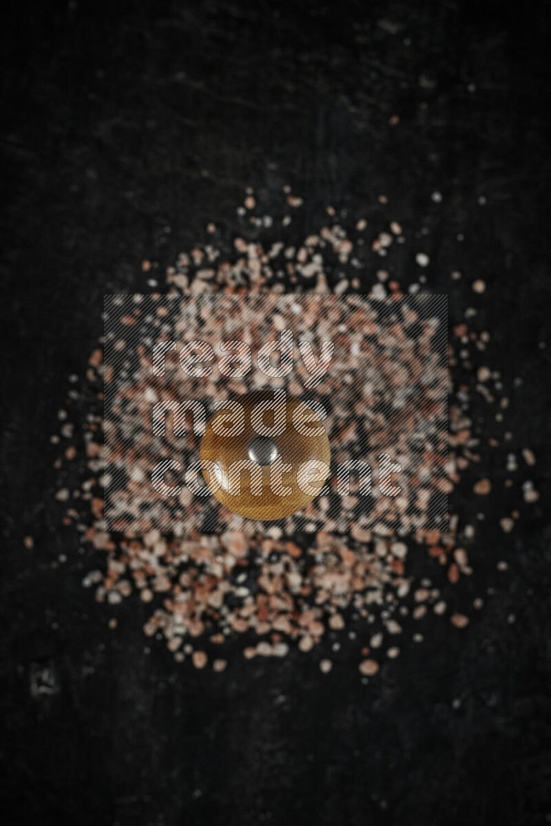 A wooden grinder standing upright and surrounded by coarse pink himalayan salt on black background