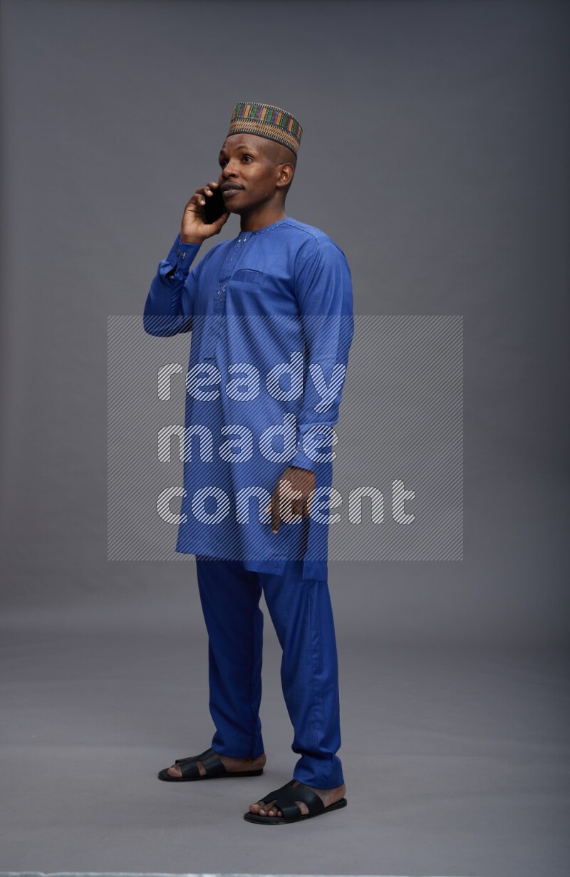 Man wearing Nigerian outfit standing talking on phone on gray background