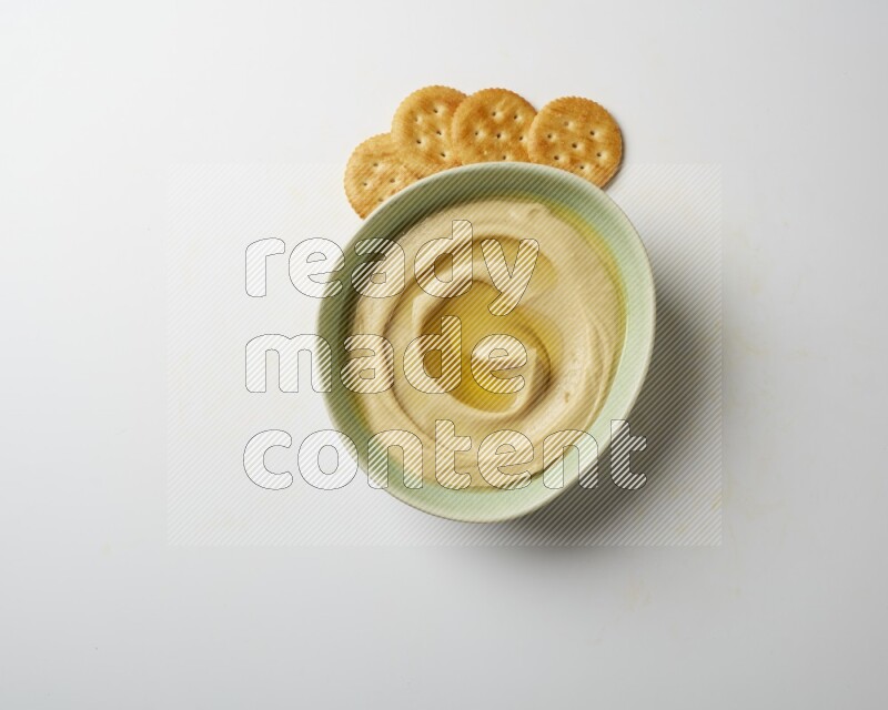 Hummus in a green plate garnished with olive oil on a white background