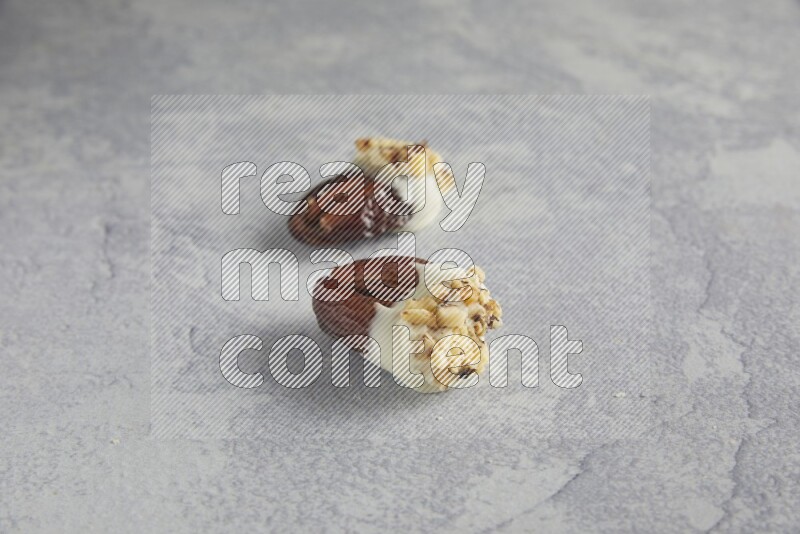 Two pecan stuffed date covered with white chocolate and chopped walnuts on alight grey background