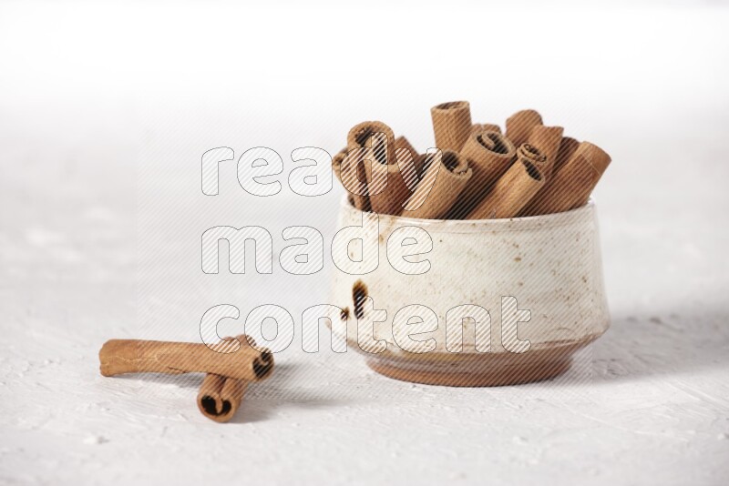 Cinnamon sticks in a beige bowl on a white background