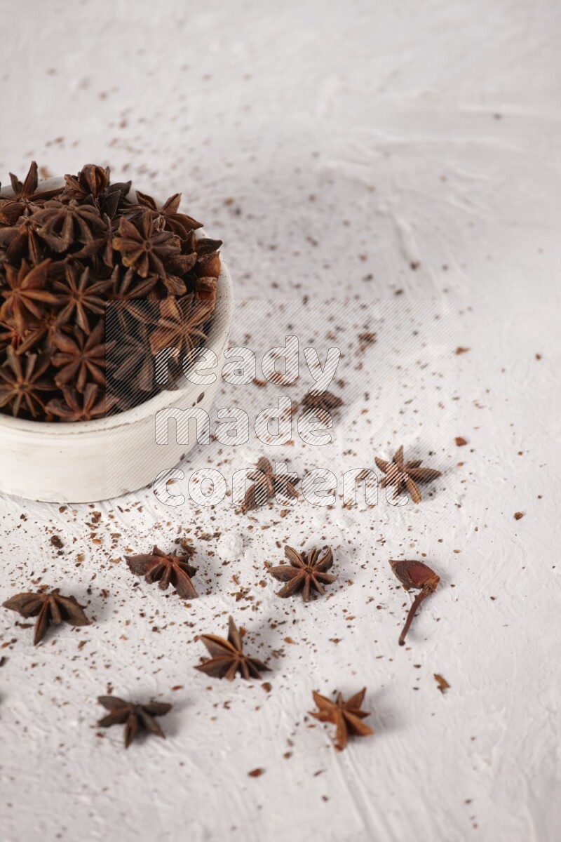 Star Anise in a white bowl and more of it sprinkled on white background