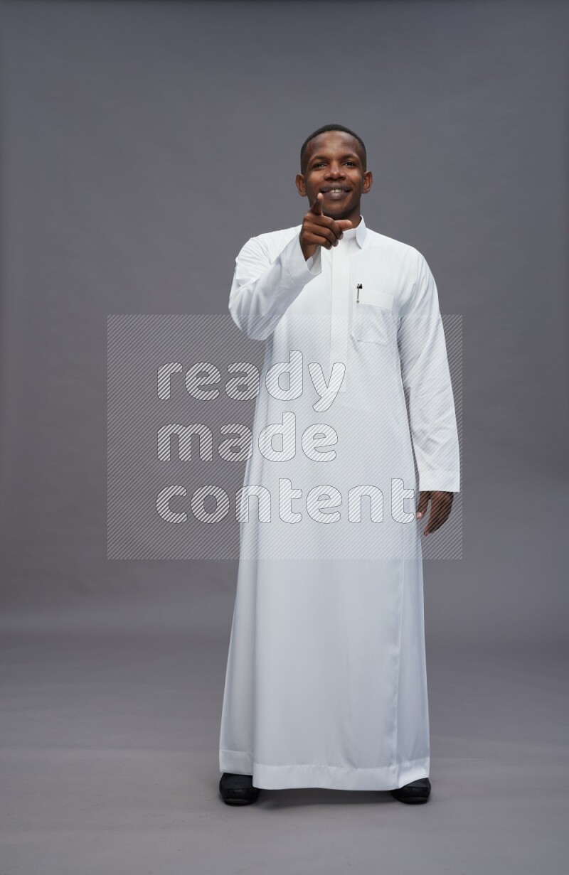 Saudi man wearing thob standing interacting with the camera on gray background