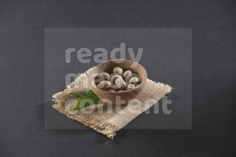 A wooden bowl full of whole nutmeg seeds on burlap fabric on a black flooring