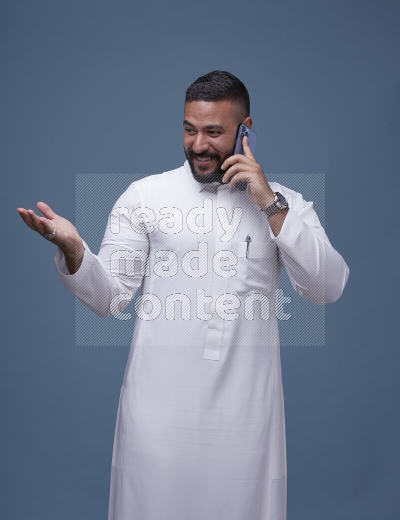 A Saudi man calling on blue background wearing Saudi Thob