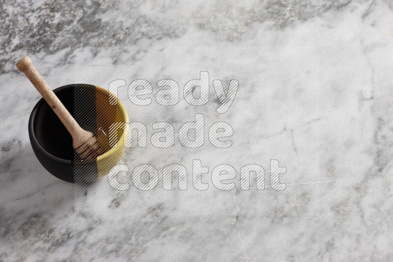 Multicolored pottery bowl with wooden honey dipper in it on grey marble background
