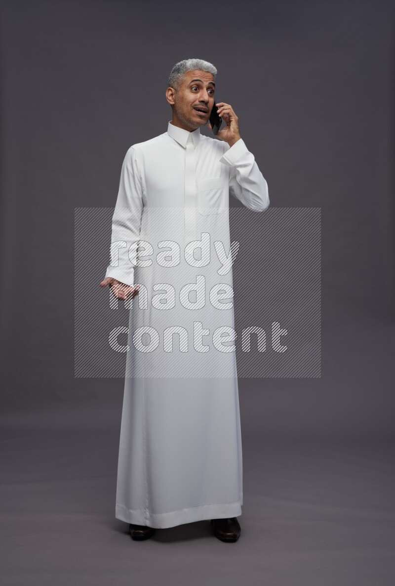 Saudi man wearing thob standing talking on phone on gray background