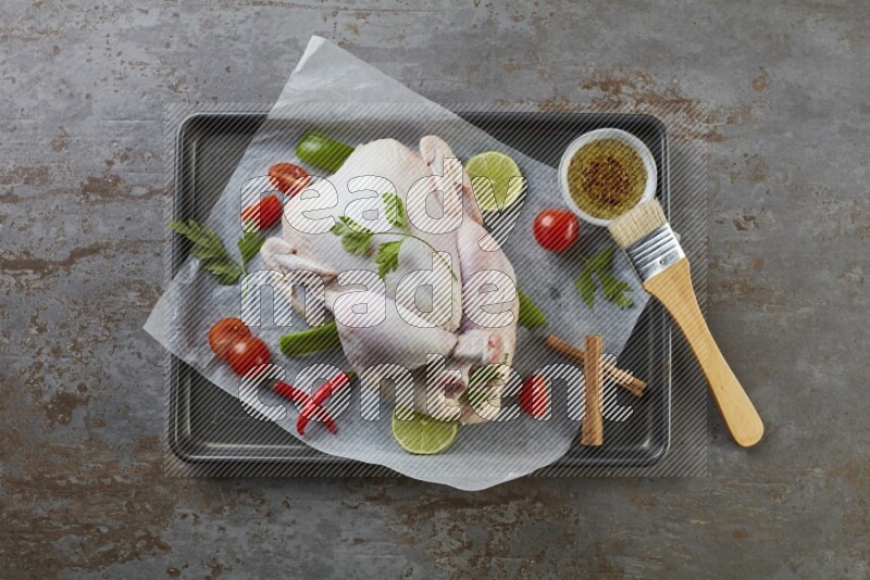 whole raw chicken on an oven trey direct on a rustic grey background