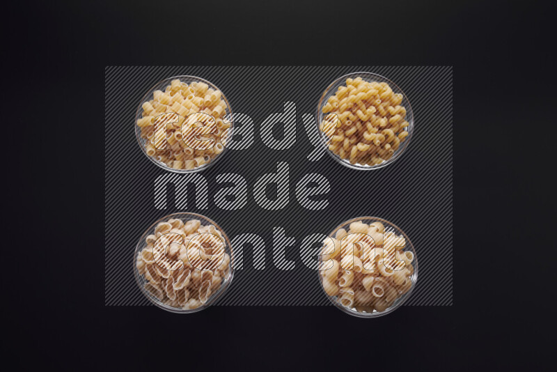 Different pasta types in glass bowls on black background