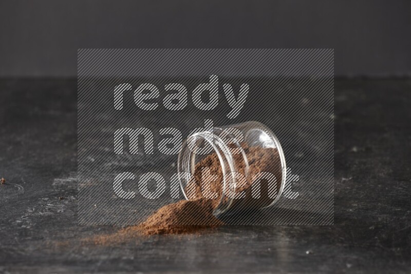 A flipped glass jar full of cloves powder on a textured black flooring