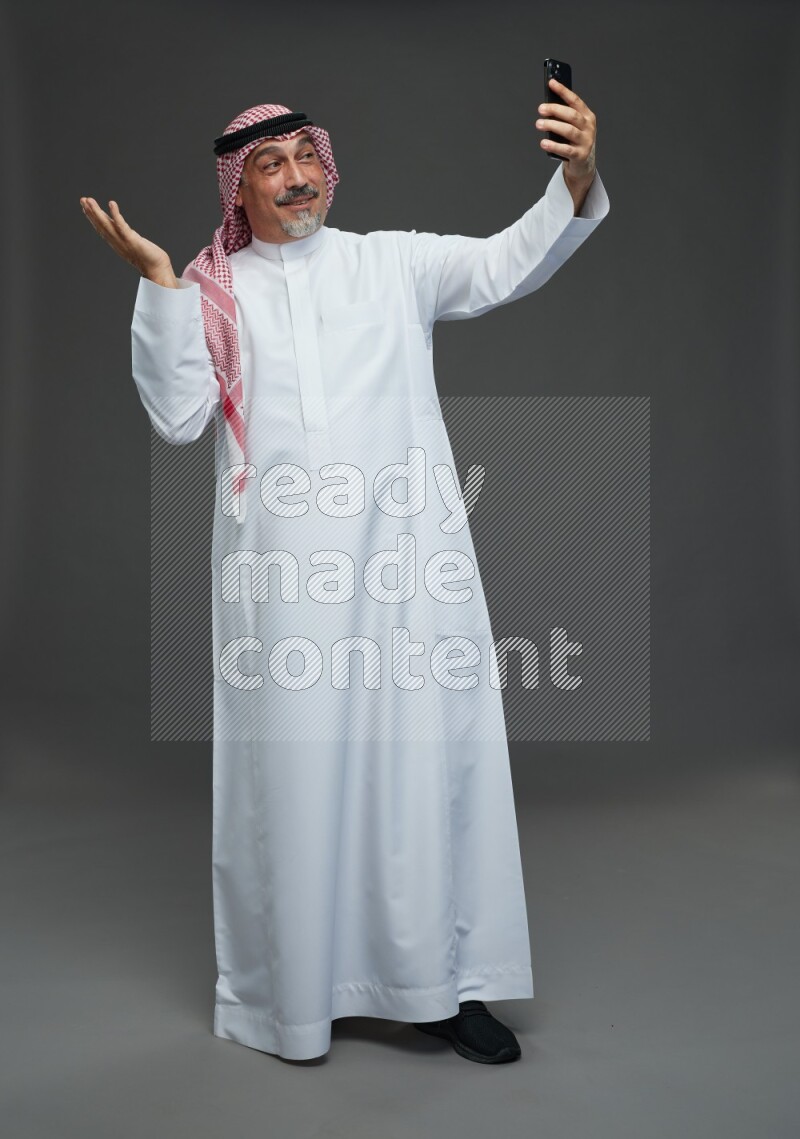 Saudi man with shomag Standing taking selfie on gray background