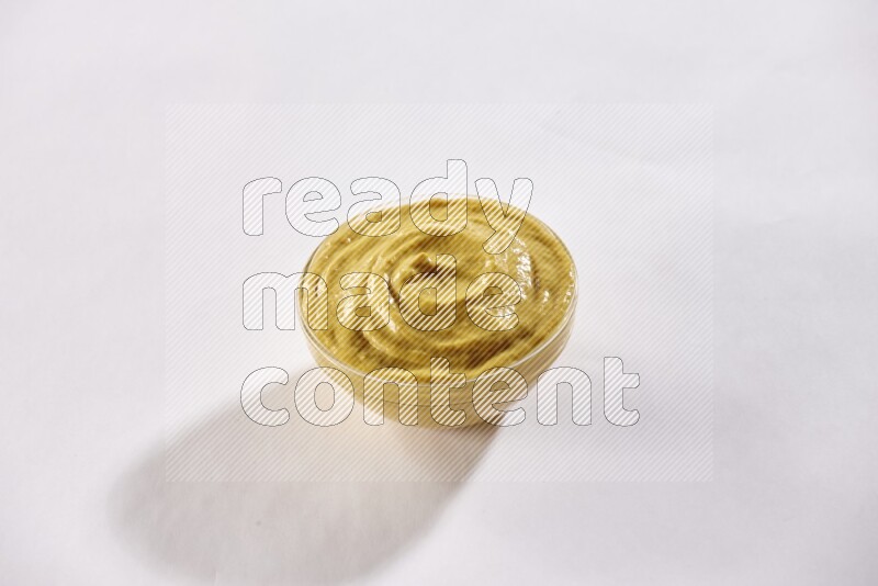 A glass bowl full of mustard paste on a white flooring