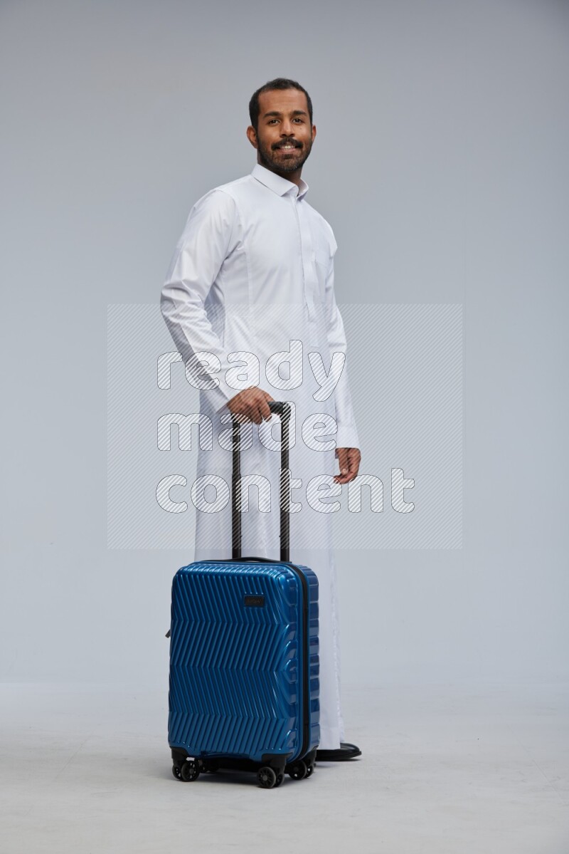 Saudi man wearing thob standing holding Travel bag on Gray background