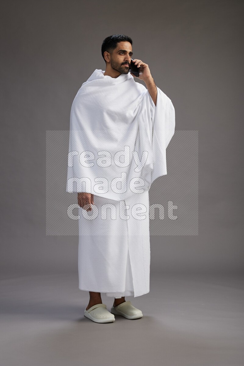 A man wearing Ehram Standing talking on phone on gray background