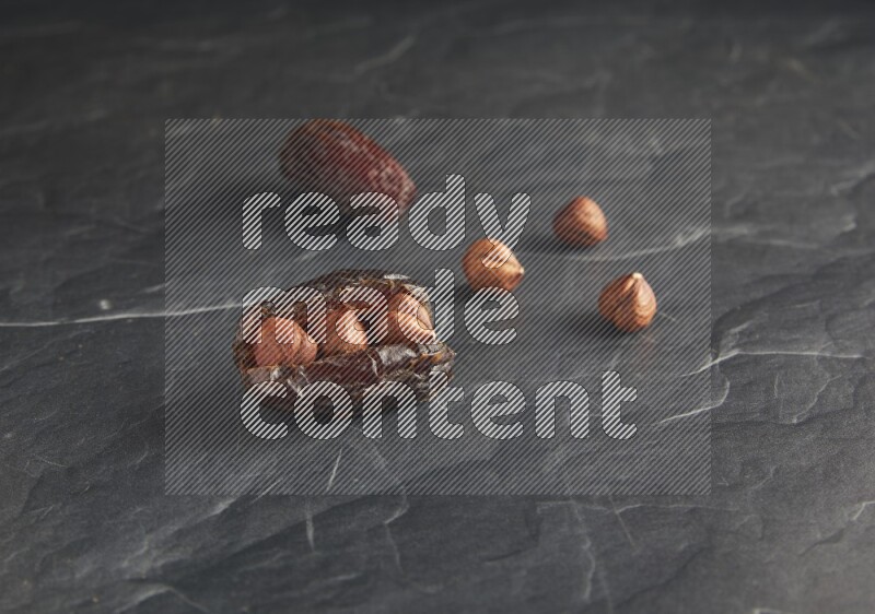 two hazelnuts stuffed madjoul dates on a black textured background