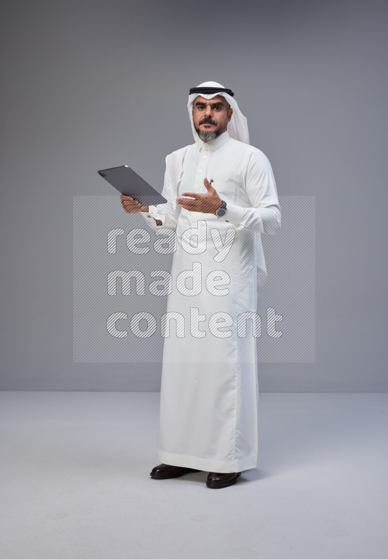 Saudi man Wearing Thob and white Shomag standing working on tablet on Gray background