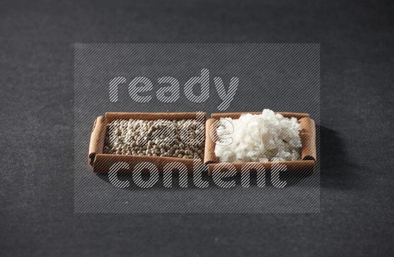 مربعان من أعواد القرفة ممتلئان بحبوب الفلفل الأسود والملح علي خلفية سوداء