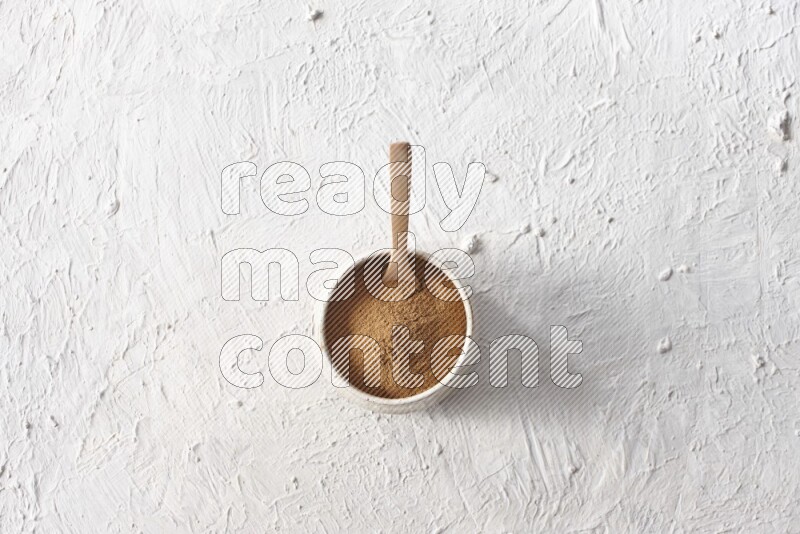 Ceramic beige bowl full of cinnamon powder with a wooden spoon on a textured white background
